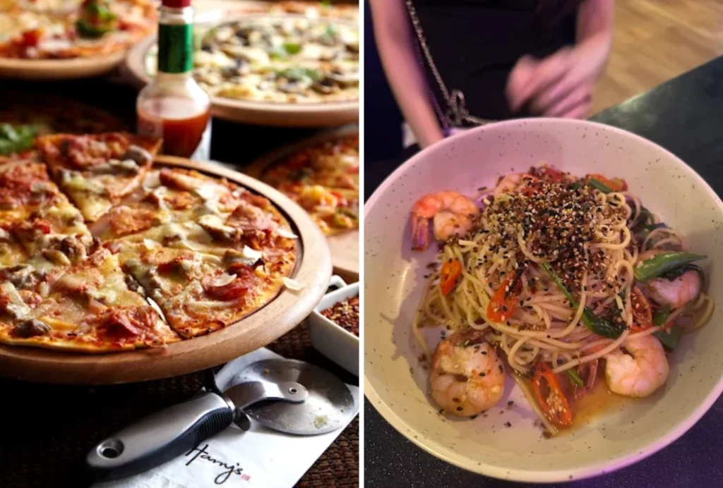 Close-up of a pepperoni and mushroom pizza on a wooden board, with a pizza and a bowl of spaghetti topped with prawns and black sesame seeds on a dark table.